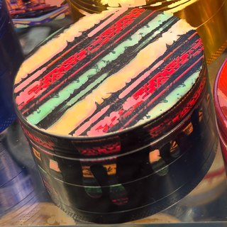 Black 4-Piece Grinder with Striped Lid Print on the shelf at Glen Smoke Shop