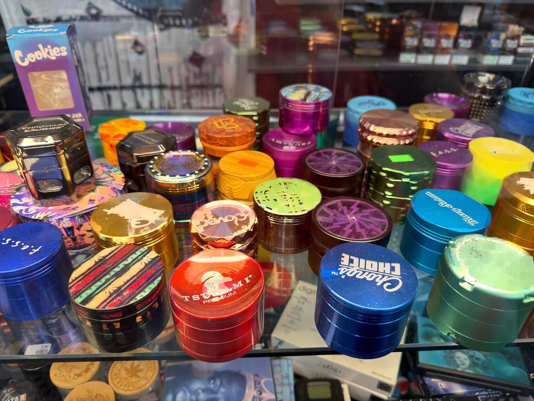 Brand-name metal grinders lined up in the lit accessories case at Glen Smoke Shop