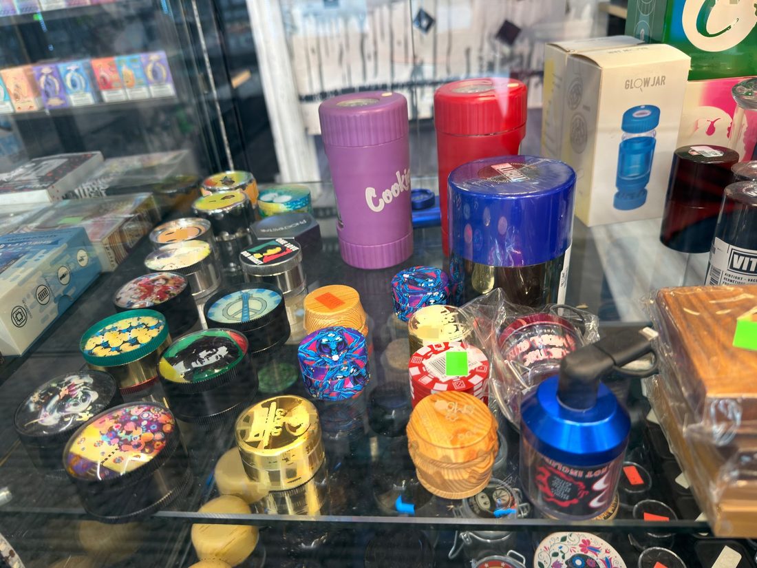 Printed-lid grinders and pocket grinders behind glass at the counter