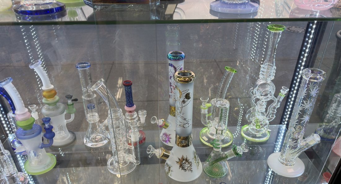 A lit display case of glass water pipes at Glen Smoke Shop, beakers and straight tubes with coloured accents