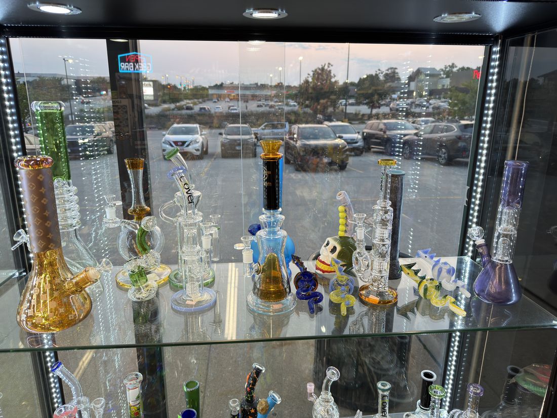 Lit case of water pipes and rigs along the front window at Glen Smoke Shop